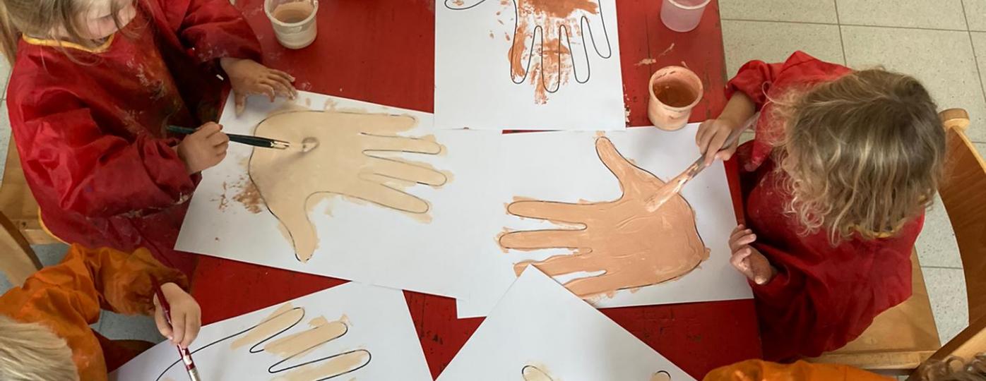 Foto van kleuters die tekeningen maken van handen in verschillende huidskleuren.